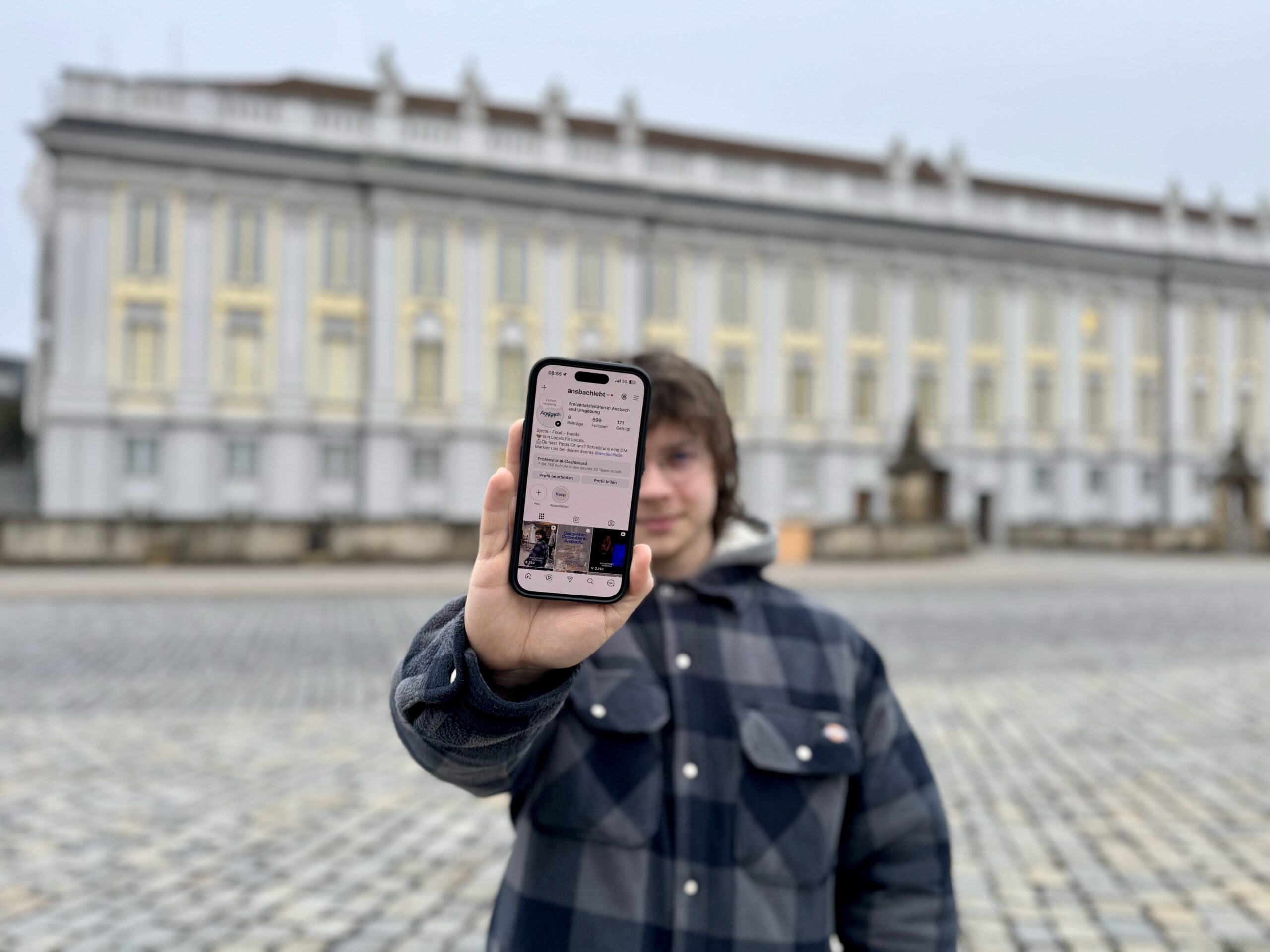 Milo von Ansbachlebt hält Smartphone in die Kamera. Er steht vor der Residenz in Ansbach.